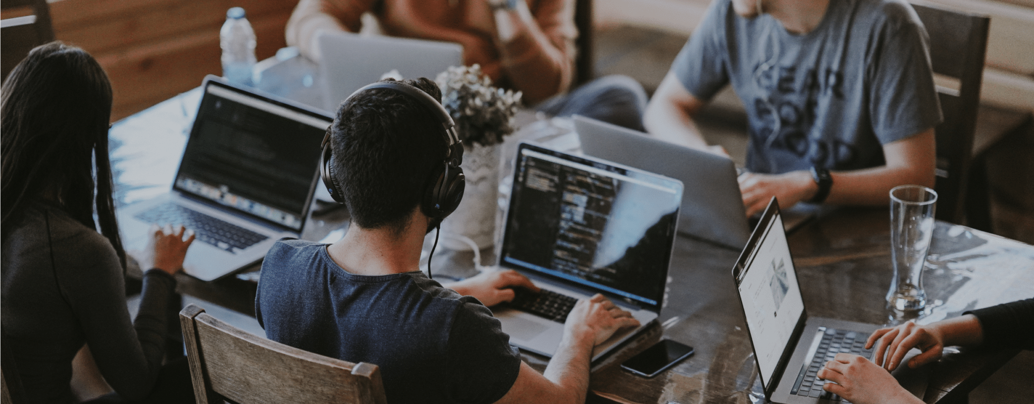 A group of people sit around a conference table with laptops open, headphones on, working on client strategy.