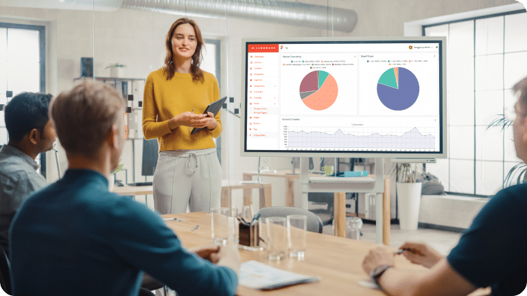 People sit around a conference table with one person standing at the front presenting Landmark reporting data.