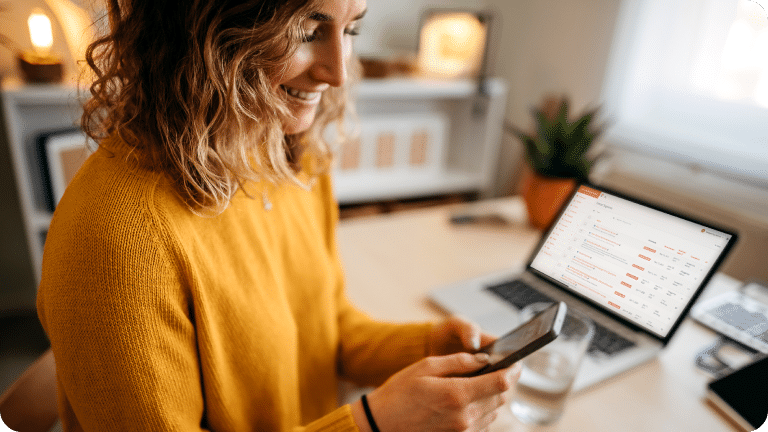 A person holds their cellphone with their laptop in the background showing Landmark email automation efforts.