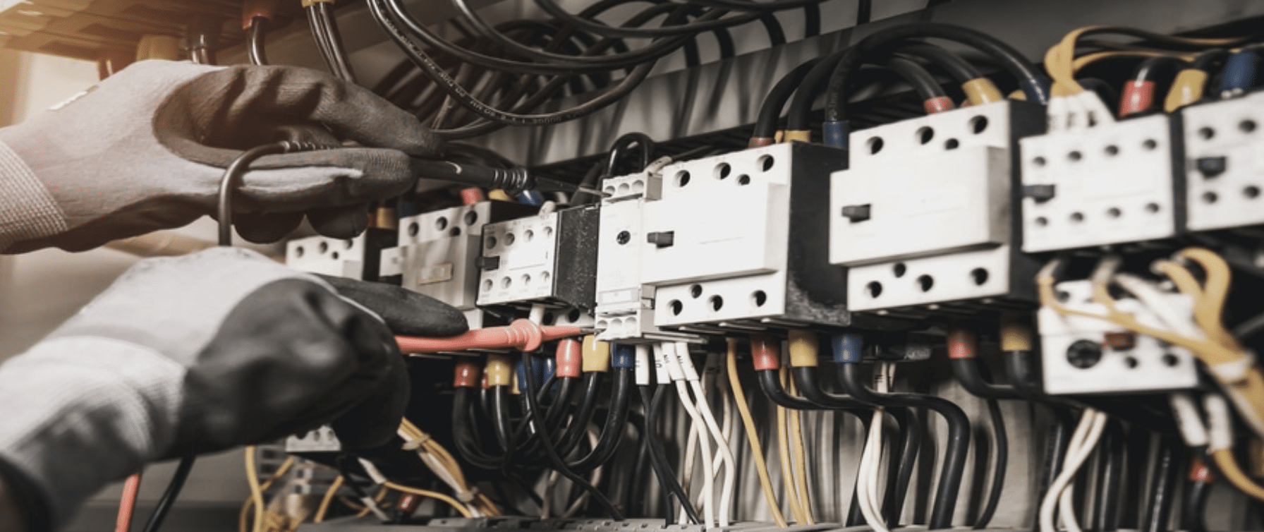 Two hands hold power supply meters up to a panel box to check power at connections.