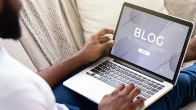 Person sits with an open laptop on their stretched out legs, while working on the Drupal website blog.