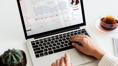 Hands lay on an open laptop keyword, with marketing data charts on the screen.