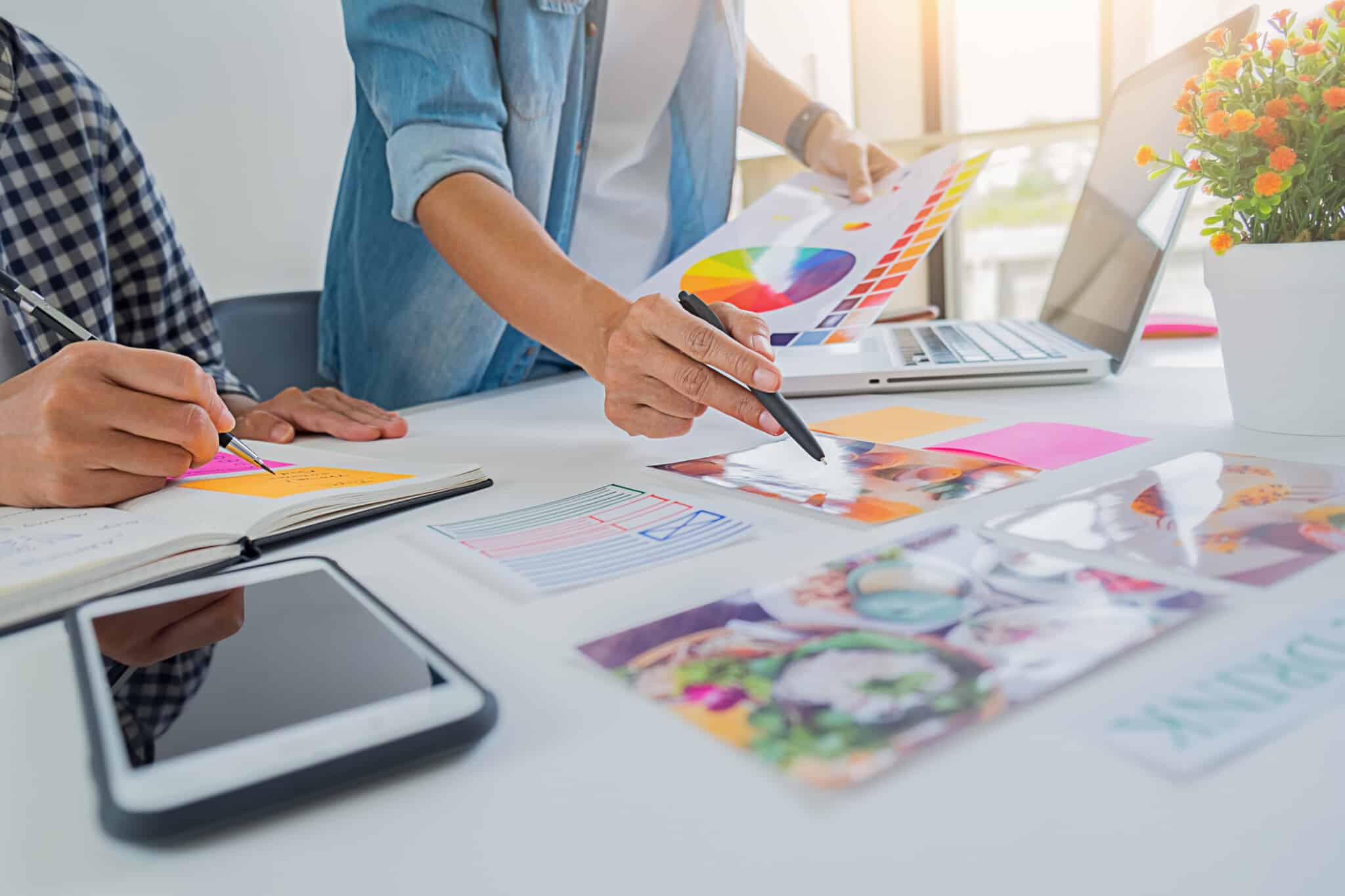 Two people at a desk with an open laptop, design materials, images, and notes create Dietitian Group website strategy.