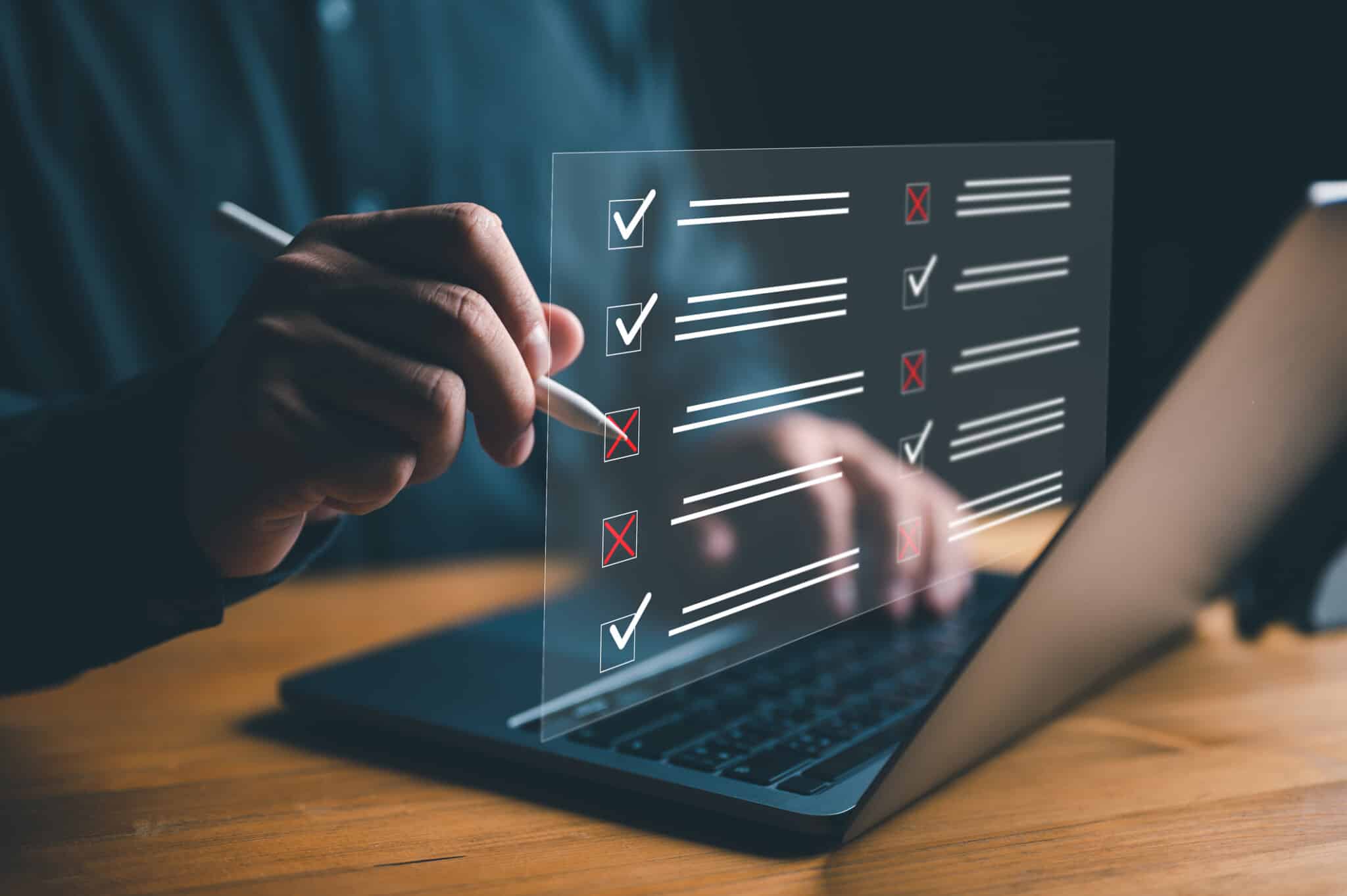Holographic checkboxes with lines hovers over an open laptop as a person 'marks' the holograph with a red x.