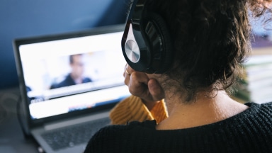 Person wearing headphones looks at an open laptop.