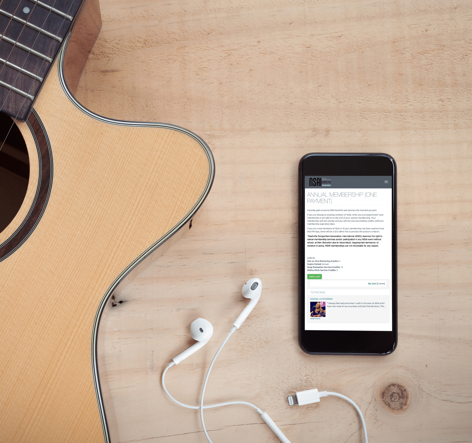 A guitar lays on the floor with headphones next to a mobile phone, showing the annual membership page of NSAI.
