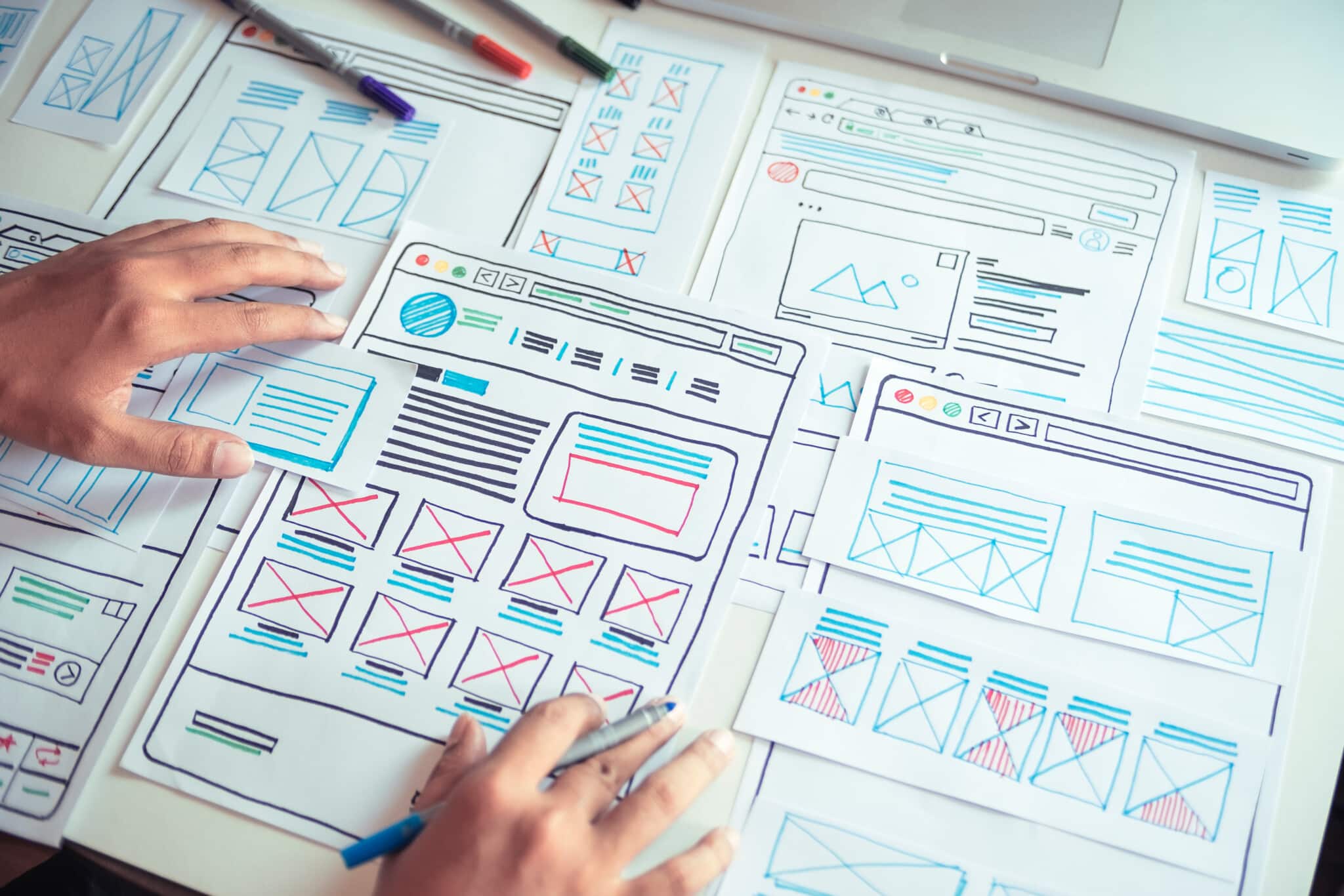 Hands sit on webpage designs with various pages and markets laid out.