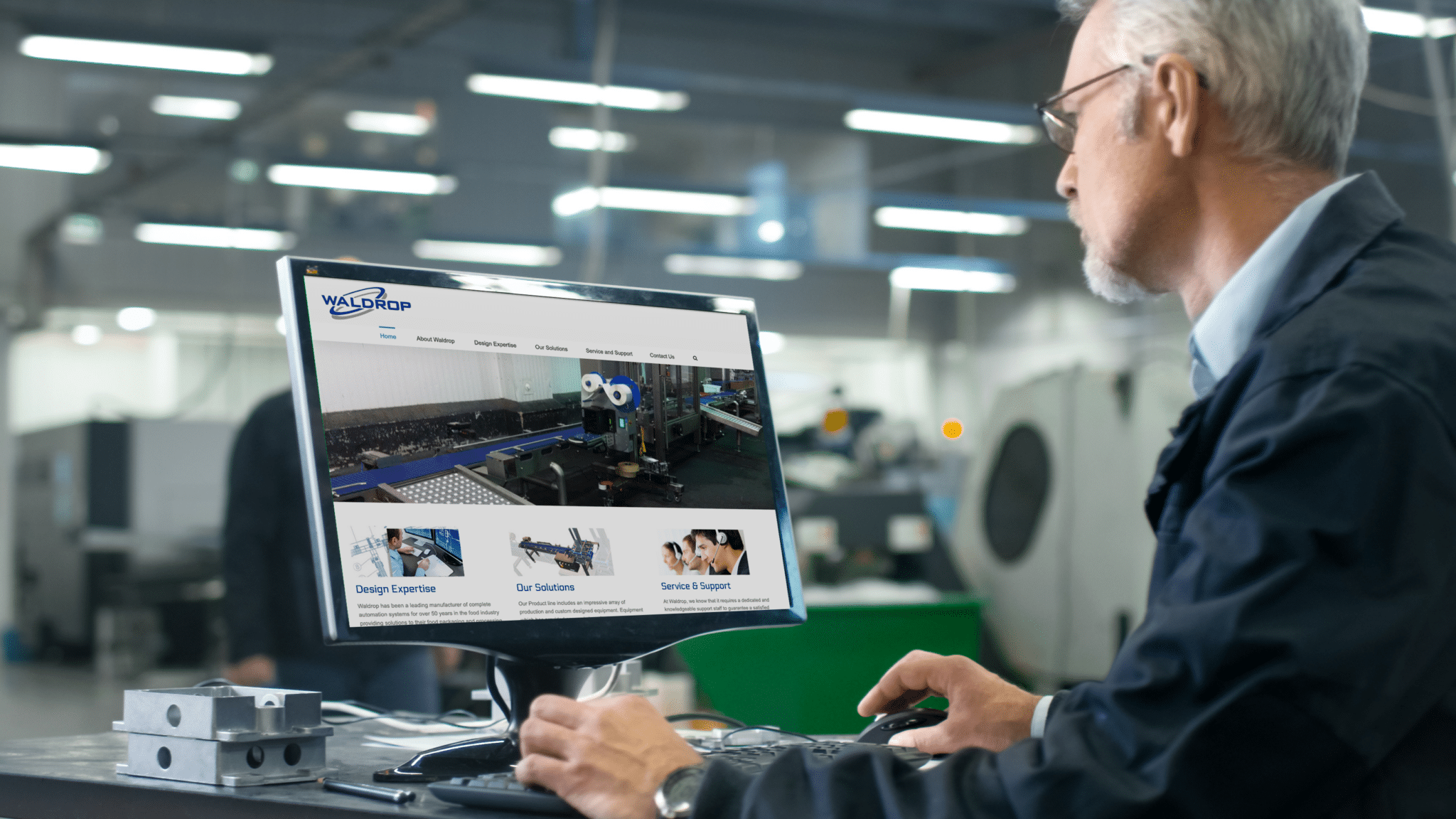 A person sits at a computer inside a manufacturing building looking at the Waldrop website.