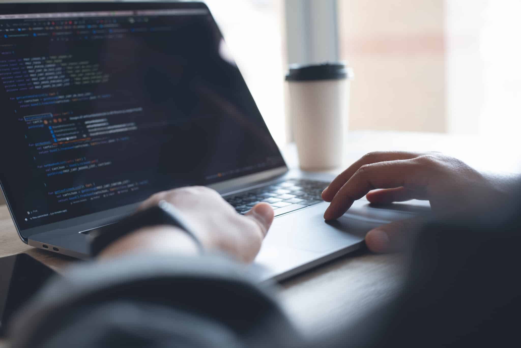 Website developer sits with an open laptop, computer code on the screen