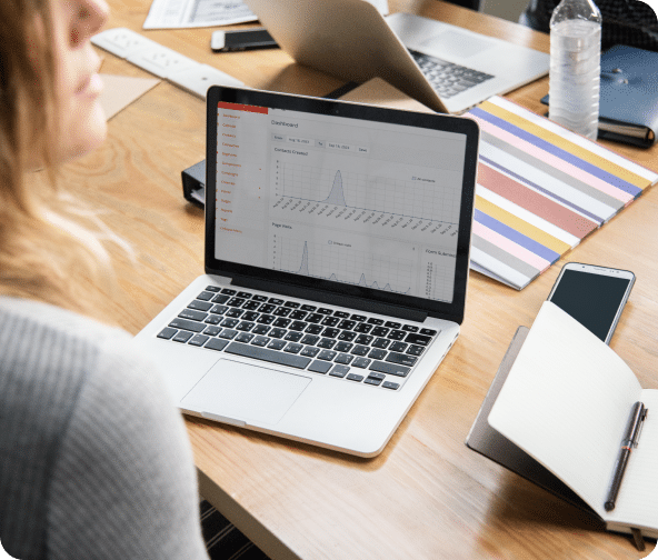 An open laptop on a desk shows Mautic metric charts as a person looks over their shoulder.
