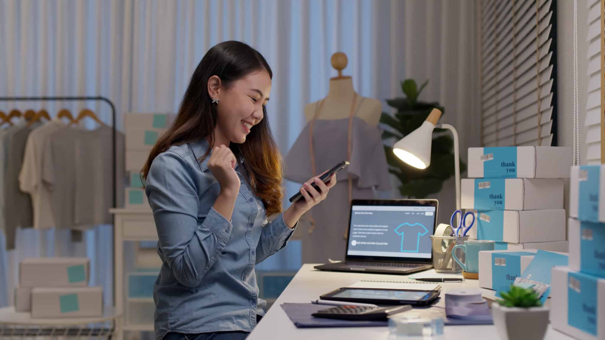 Person sits with mobile in hand and laptop in front of them looking at eCommerce themes.