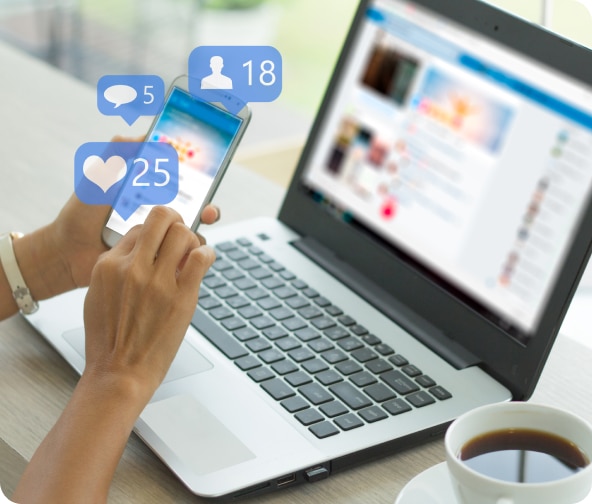 Person sits with mobile phone in hand, laptop on desk, looking at social media digital ad options.