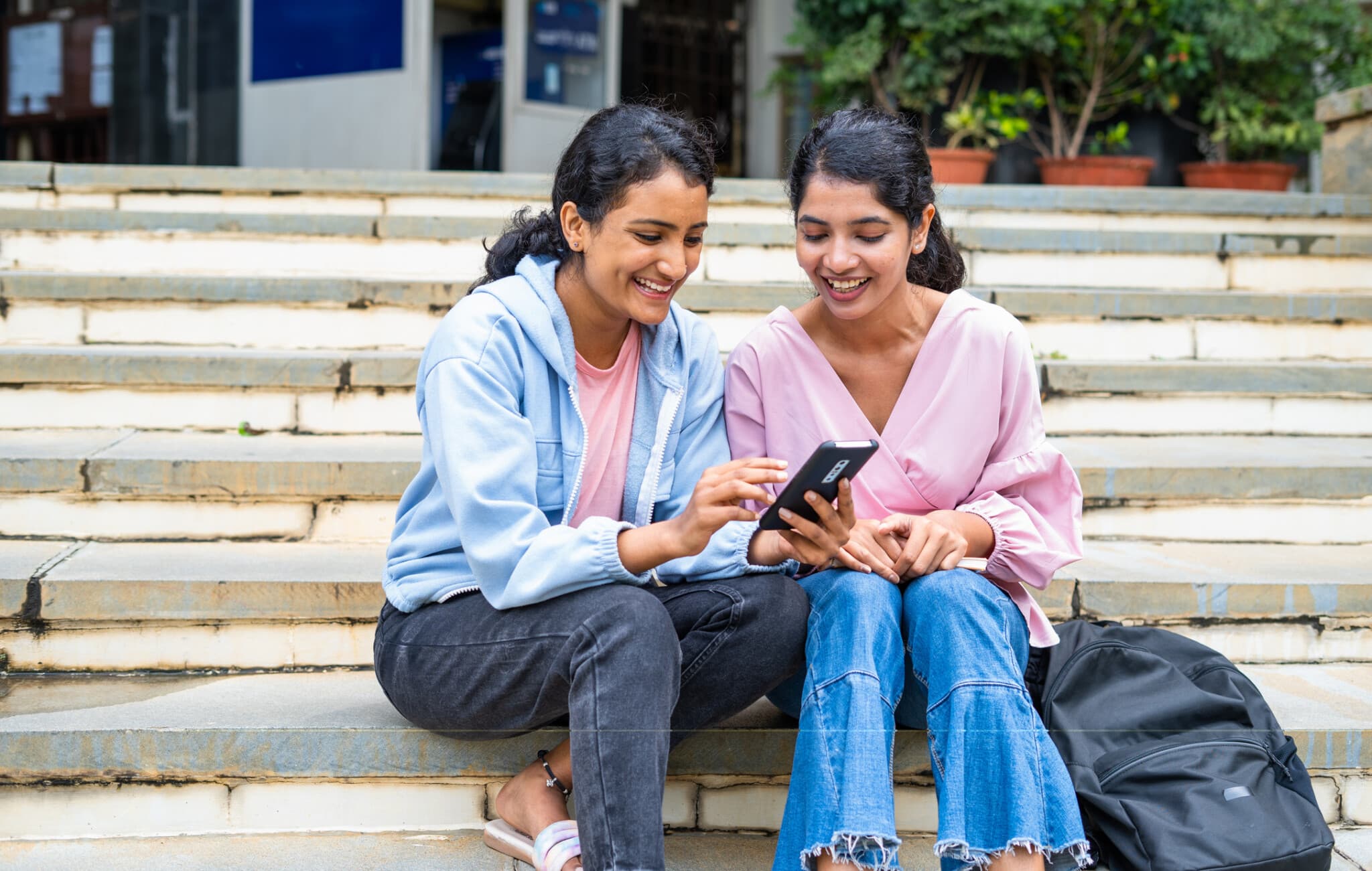 Student sit on steps looking at a mobile phone for school updates.
