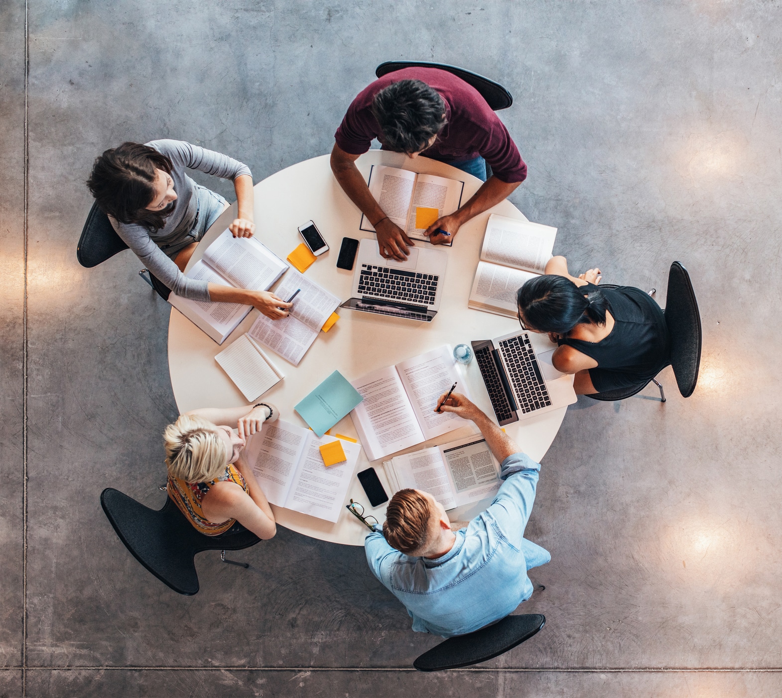 A group of student sit around a table, laptops and notes in front of them, as they study.