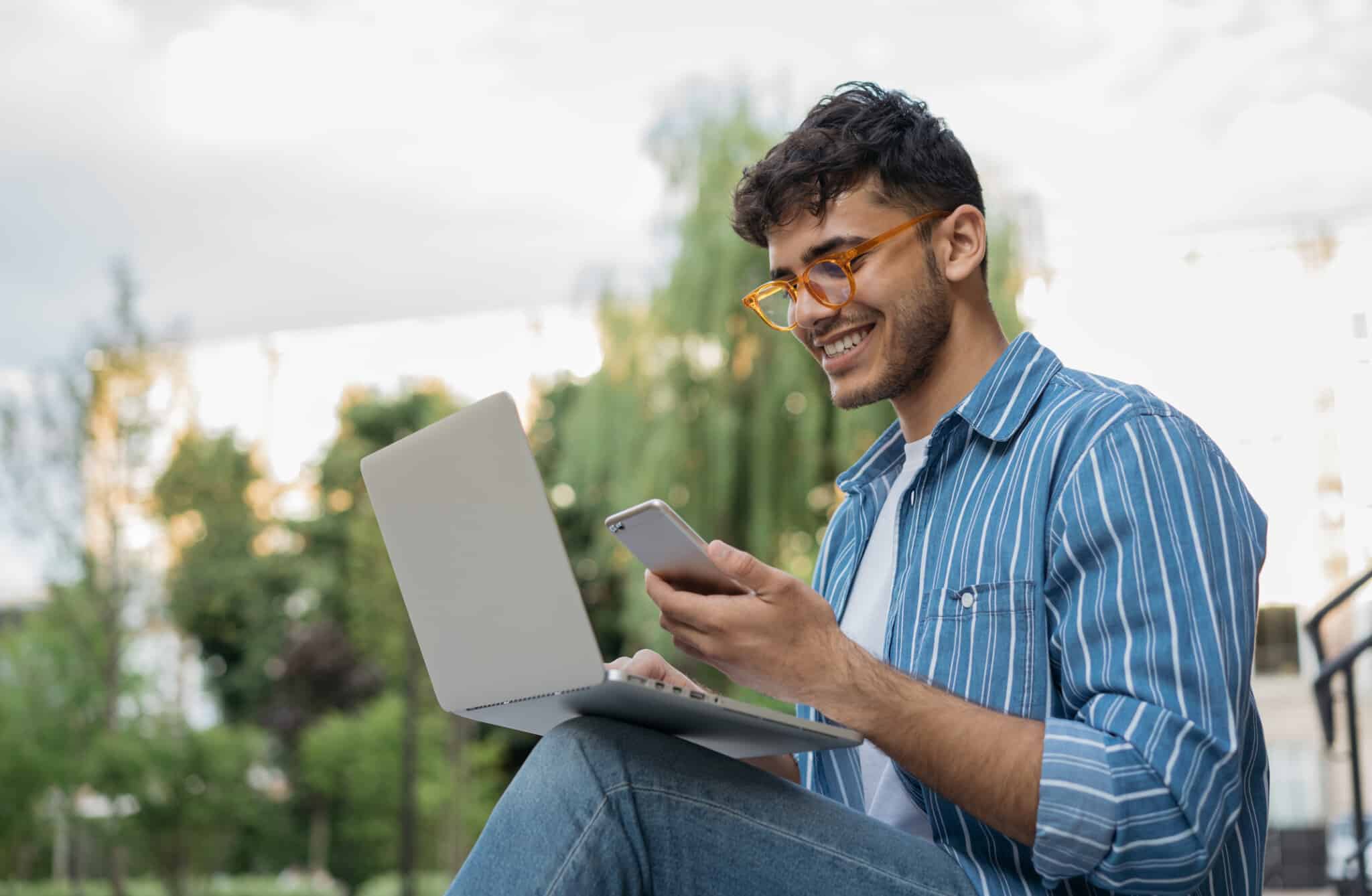 Person sitting outside with laptop on lap and mobile in hand chatting with Plan Left Augment Team.