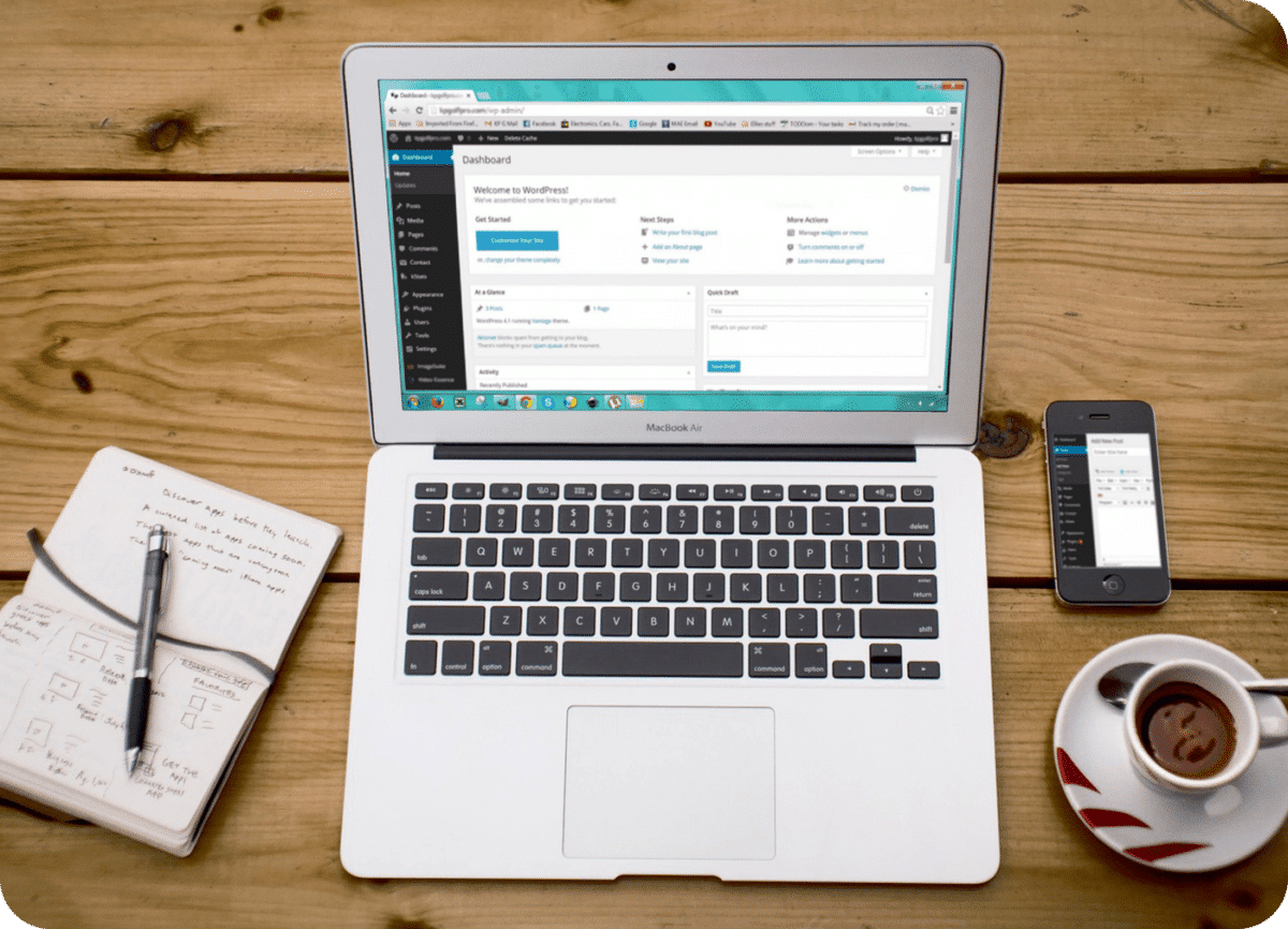 WordPress backend home screen shown on a laptop with a cup of coffee and notepad next to it.