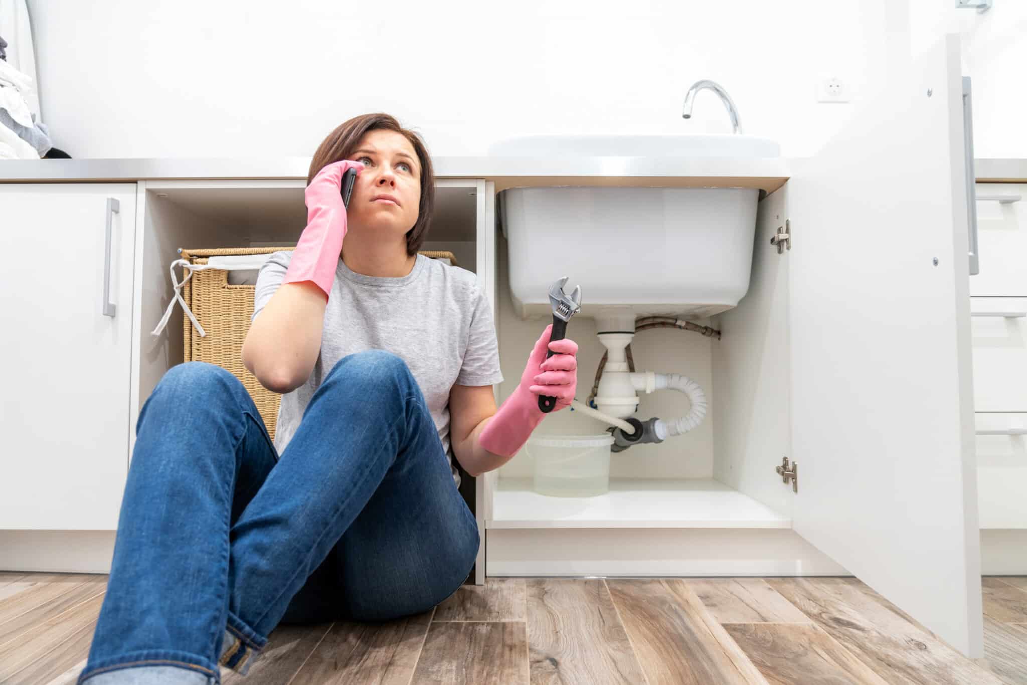 Person sits in front of a broken sink calling a local plumber.