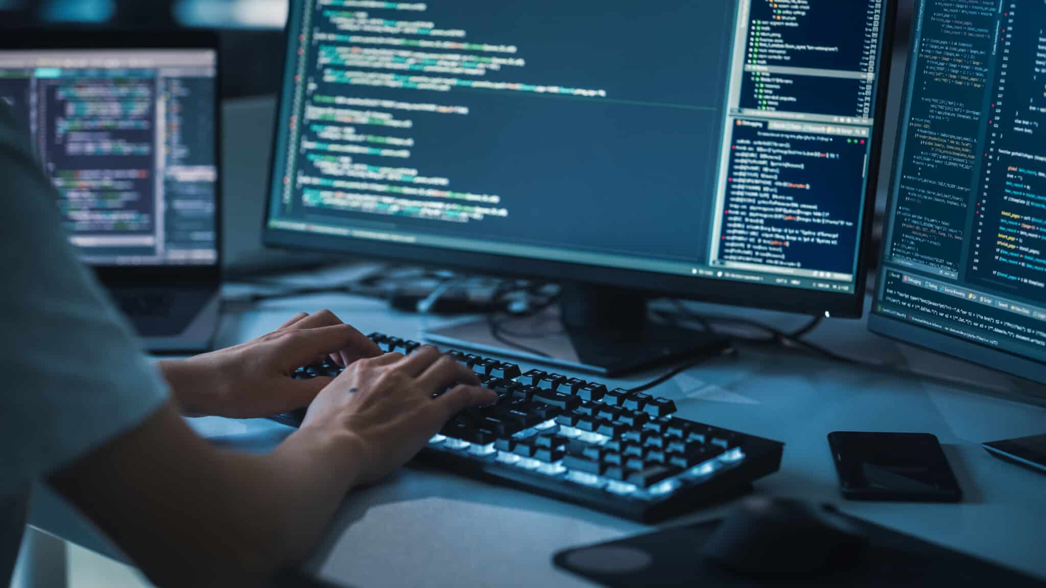 Person types website code on their keyboard with the monitor displaying the backend details.