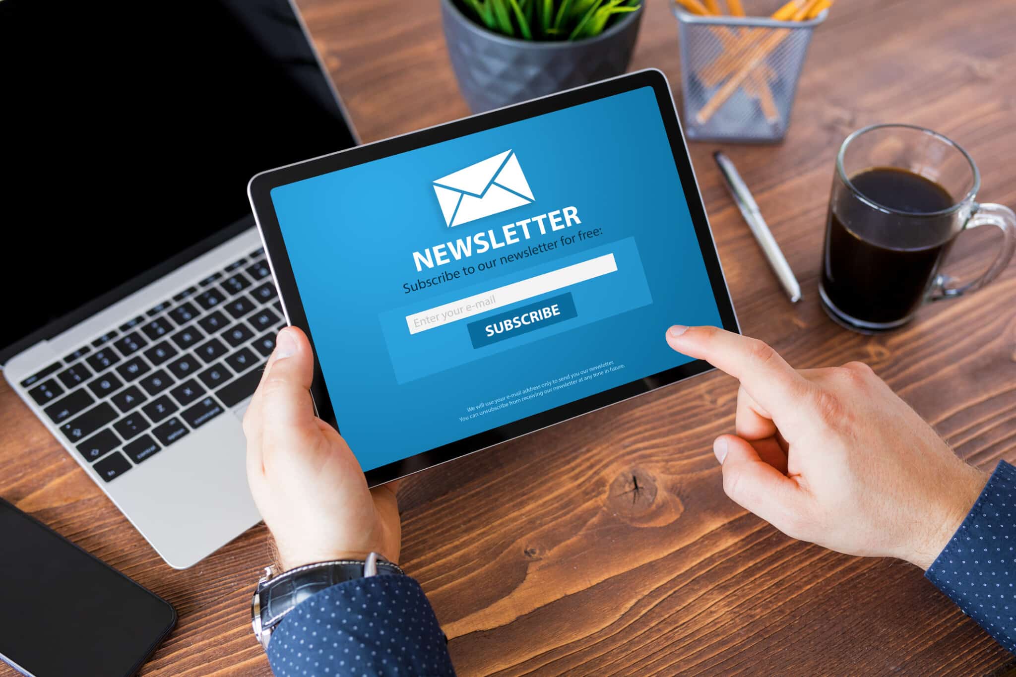 Person reading newsletter signup page on tablet with a laptop behind it.