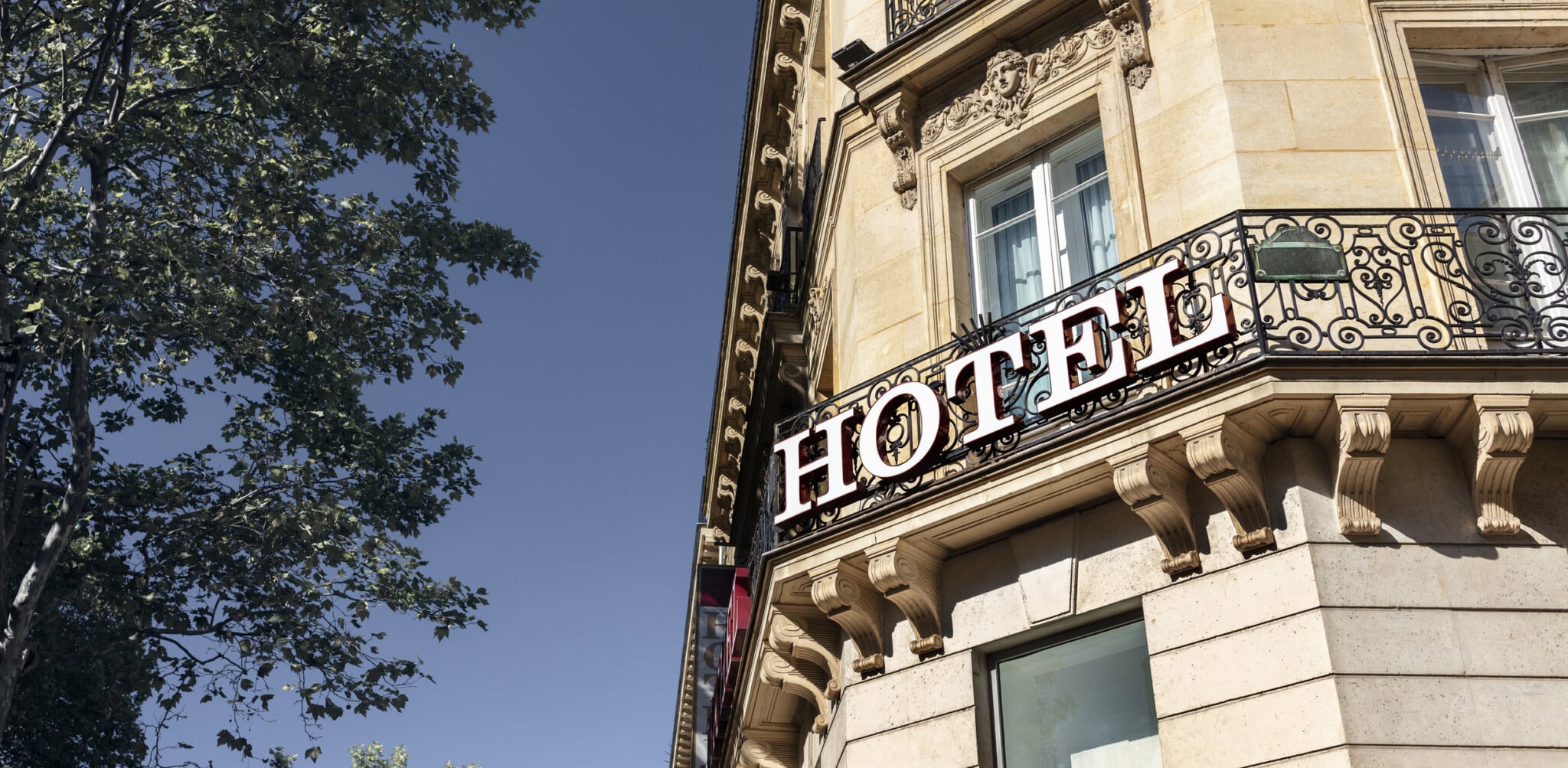 Old building with Hotel sign on the front, shaded by a large tree on the side.