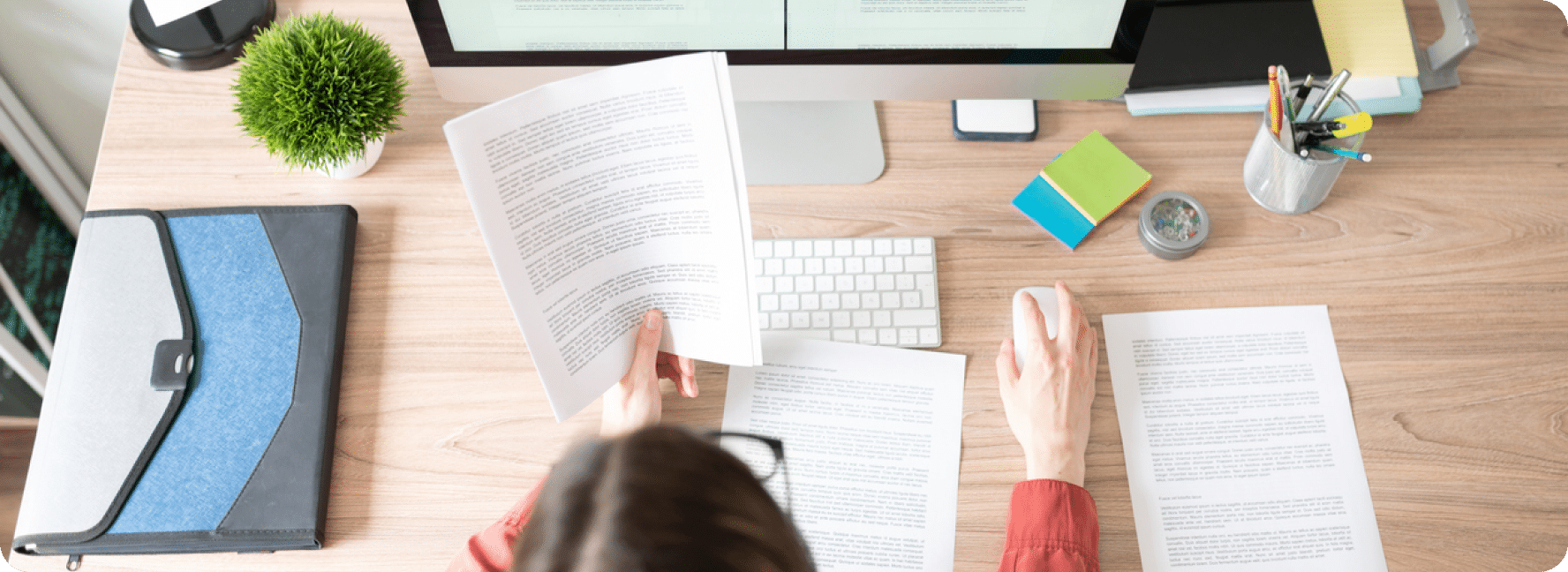 Person sits holding a paper with their computer in front of them as they quality check the website content.