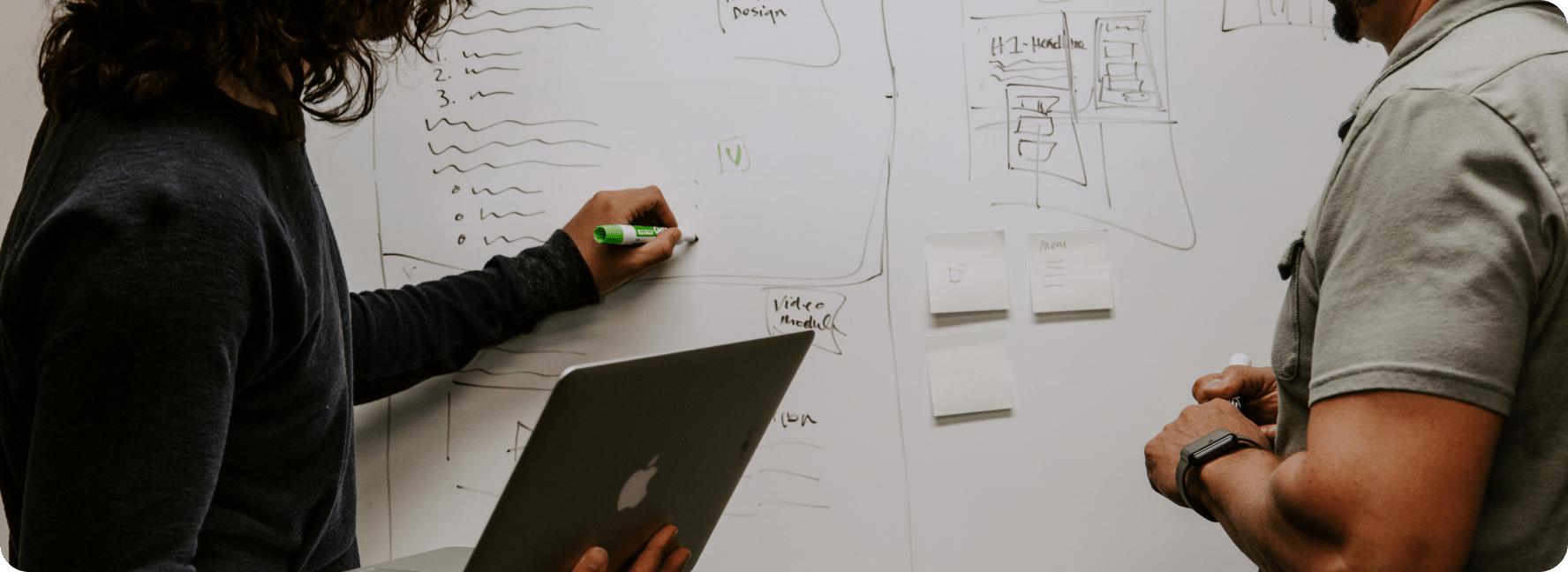 Two people stand at a white board with papers and drawings for content strategy.