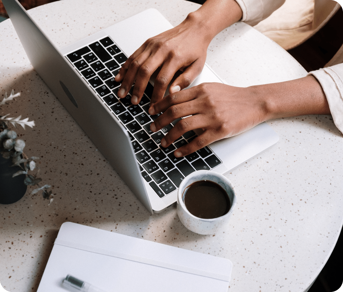 Two hands on a laptop keyboard with a coffee cup next to it.