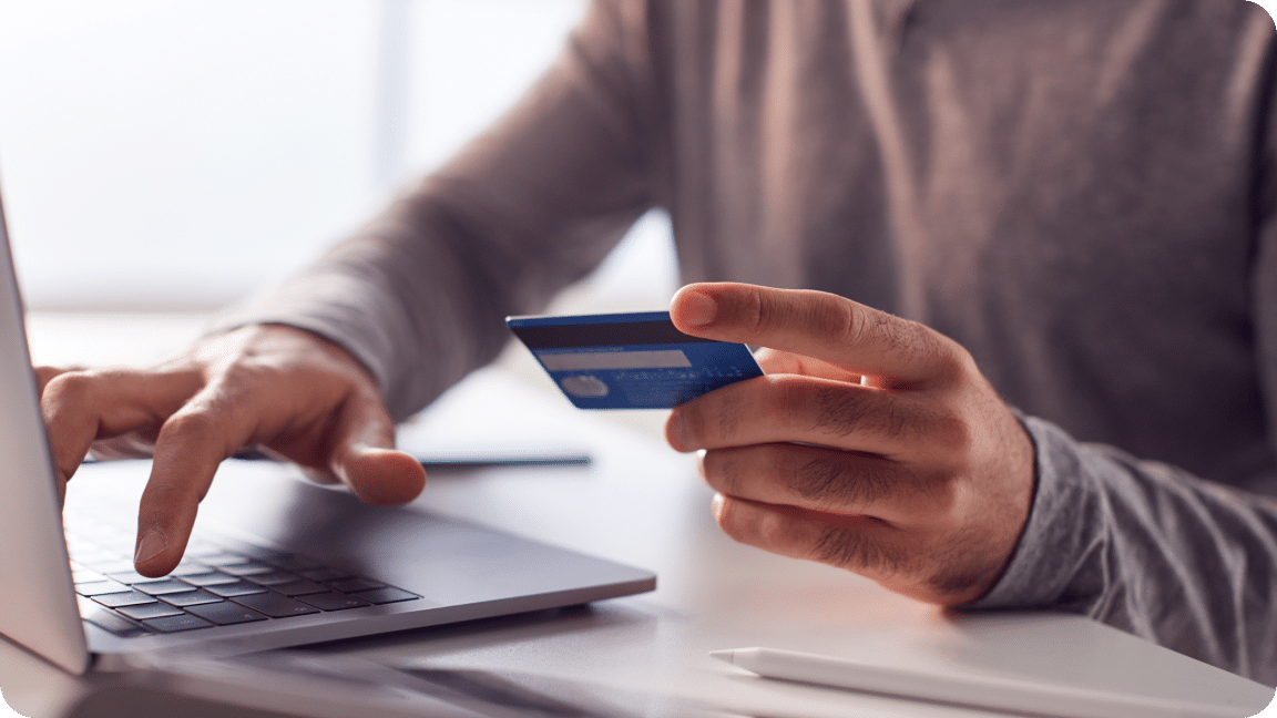 Card in one hand, the other hand typing on a keyboard as the person makes a purchase.