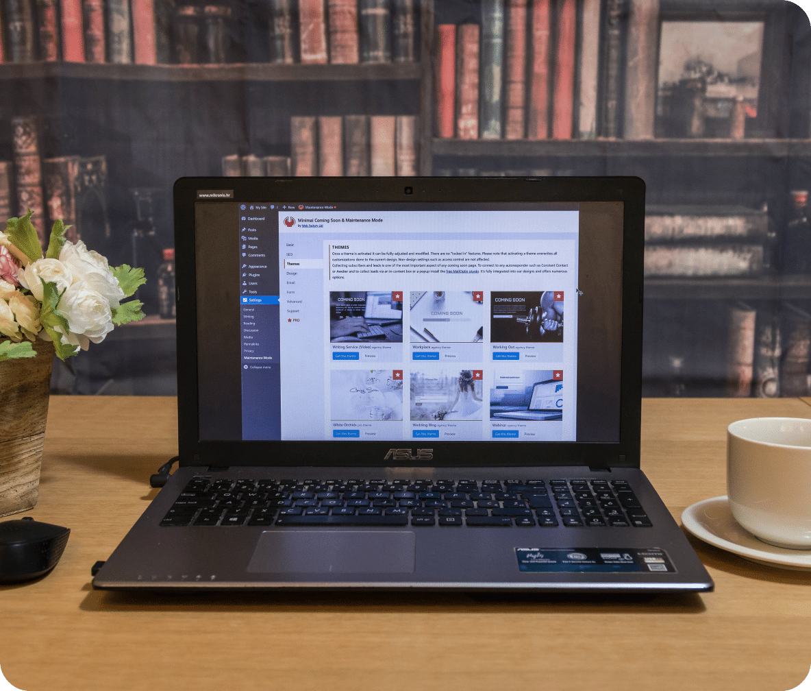 Books sit on shelves behind an open laptop with a WordPress web page in development.