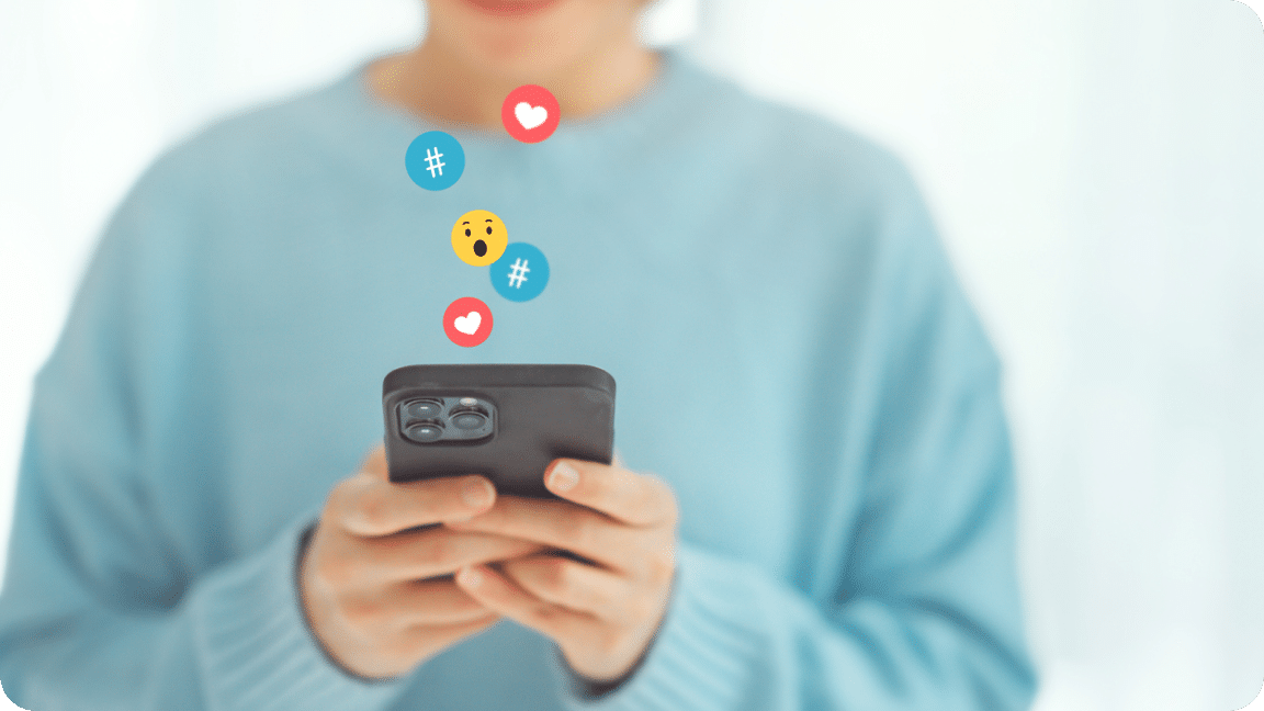 Various emojis appear to float above a cellphone as a user looks at their phone.