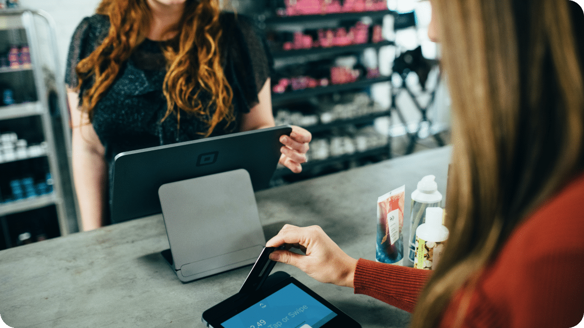 Two people stand at a counter, one paying for a purchase and the other looking at a screen.