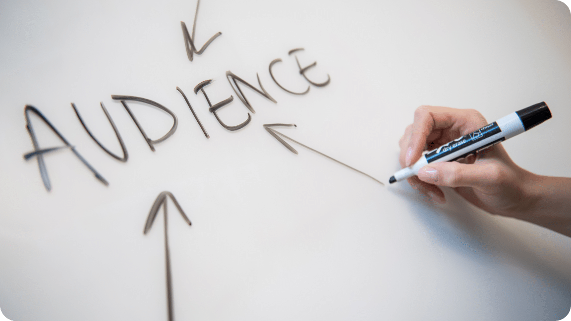Hand holds a dry erase marker as they draw an arrow to the word audience.
