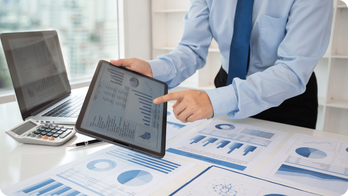 Person shows a tablet with monthly reporting data and printed materials on scattered below.