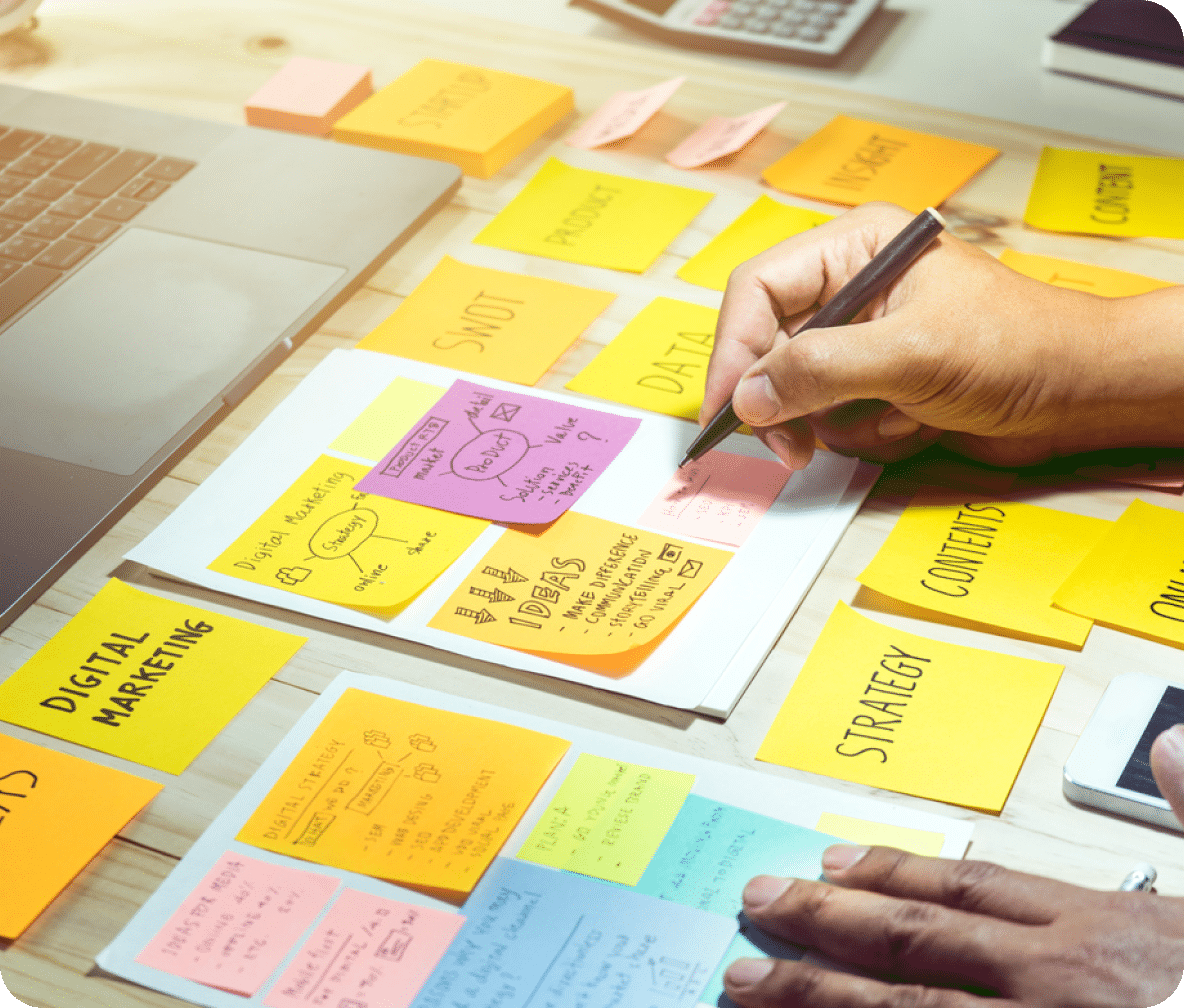 Strategy notes scattered across a desk with a laptop and calculator in the background.