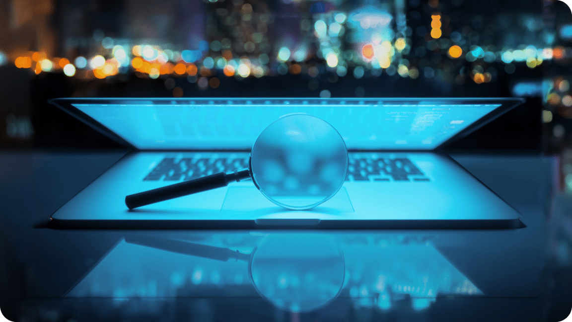 Dark background with a half-closed laptop, magnifying glass between the keyboard and lid.