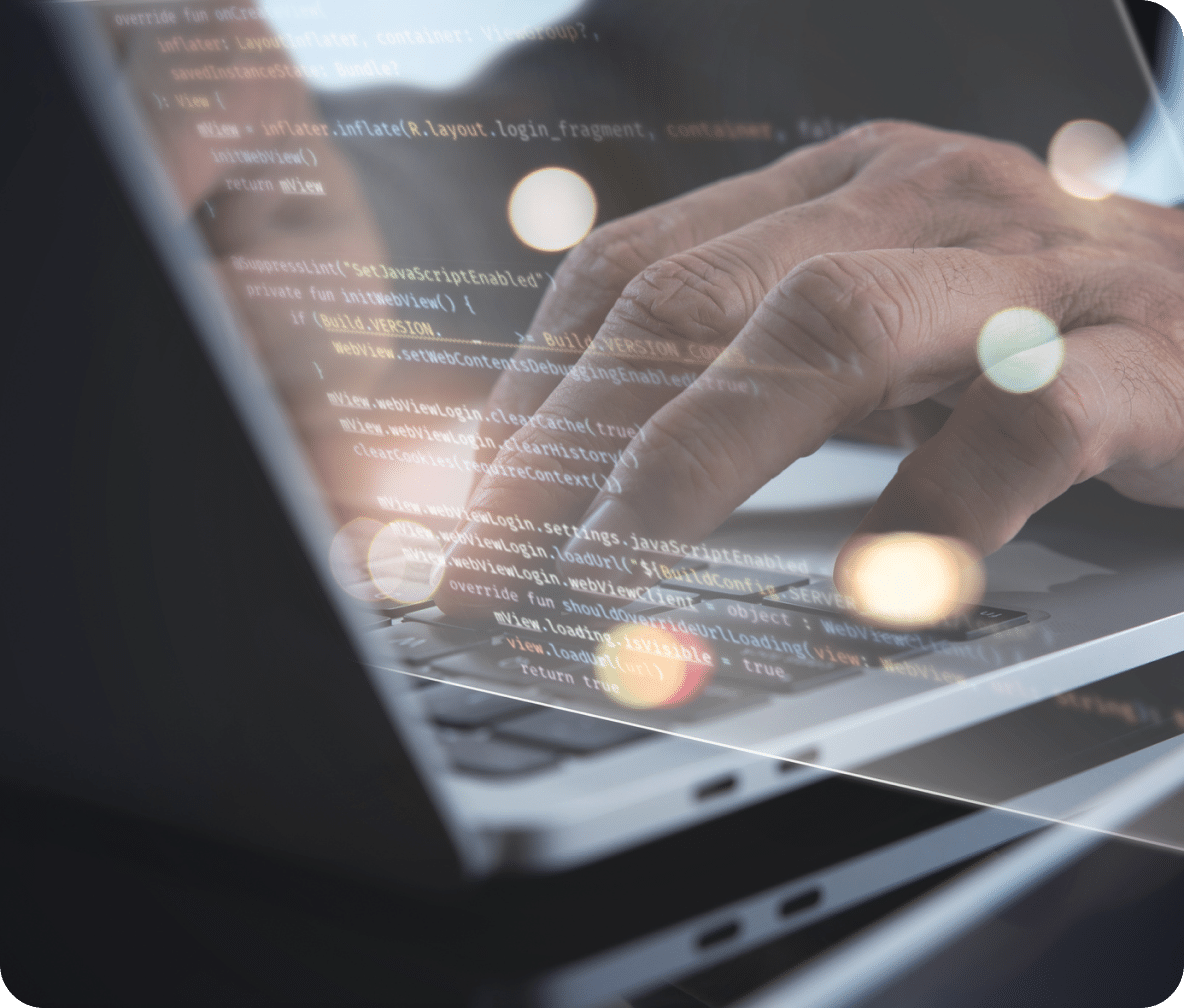 Hands type on a laptop keyboard with a screen protector reflecting rows of website code.