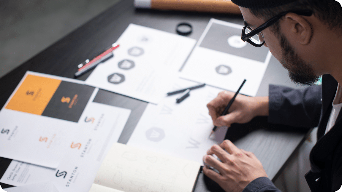 Person sits at their desk reviewing designs, marking edits and notes.