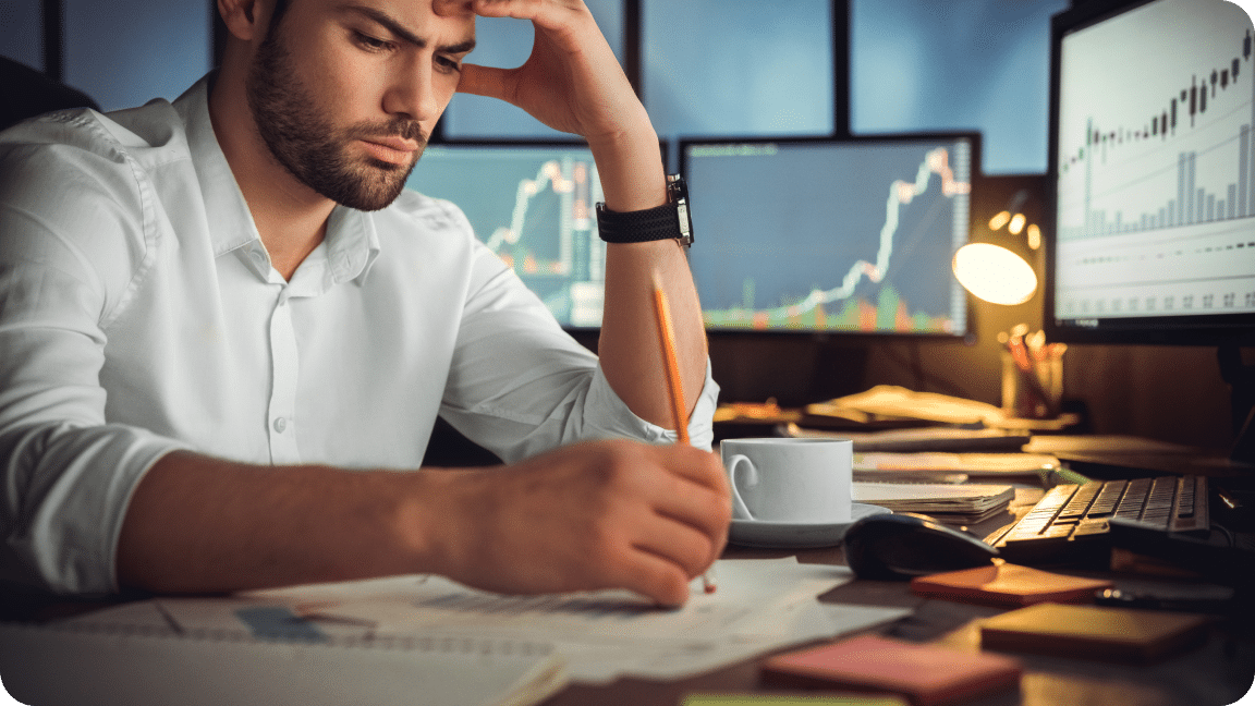 Person sits with their head in their hand and writing notes on data sheets with the other hand.