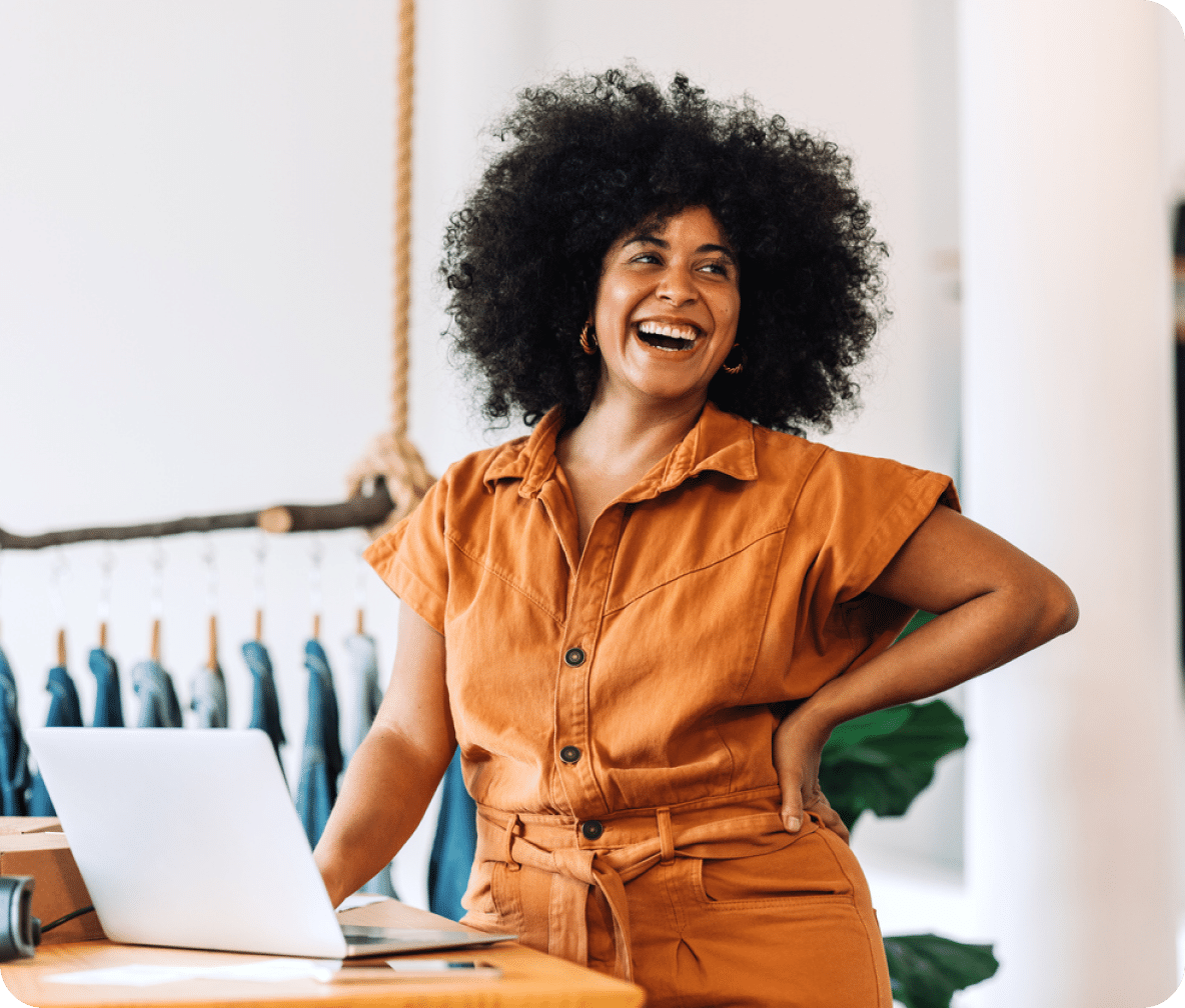 Smiling, a person stands at their counter with an open laptop in front of them.