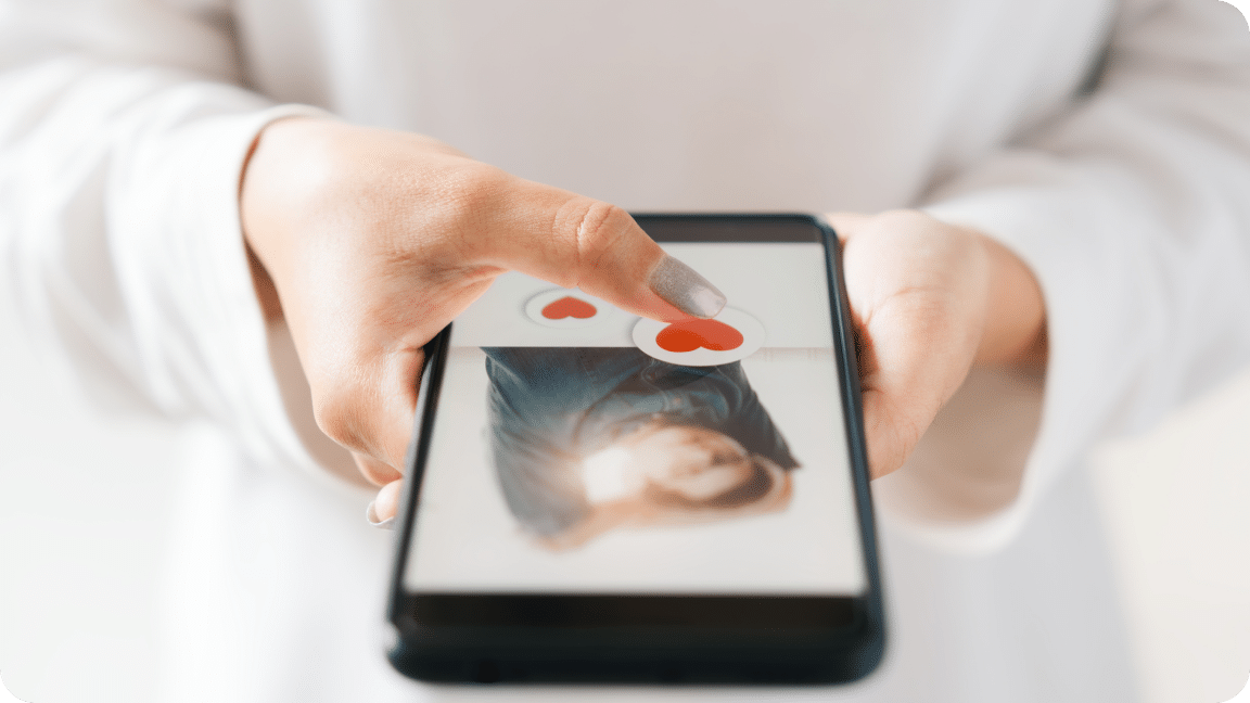 Two hand hold a mobile device, with one handing adding hearts on an image.