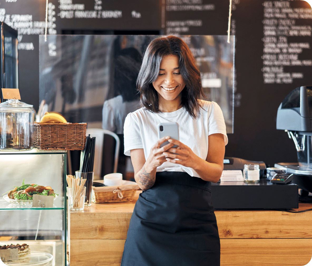 Business owners leans again their deli count, with their smartphone in their hands.