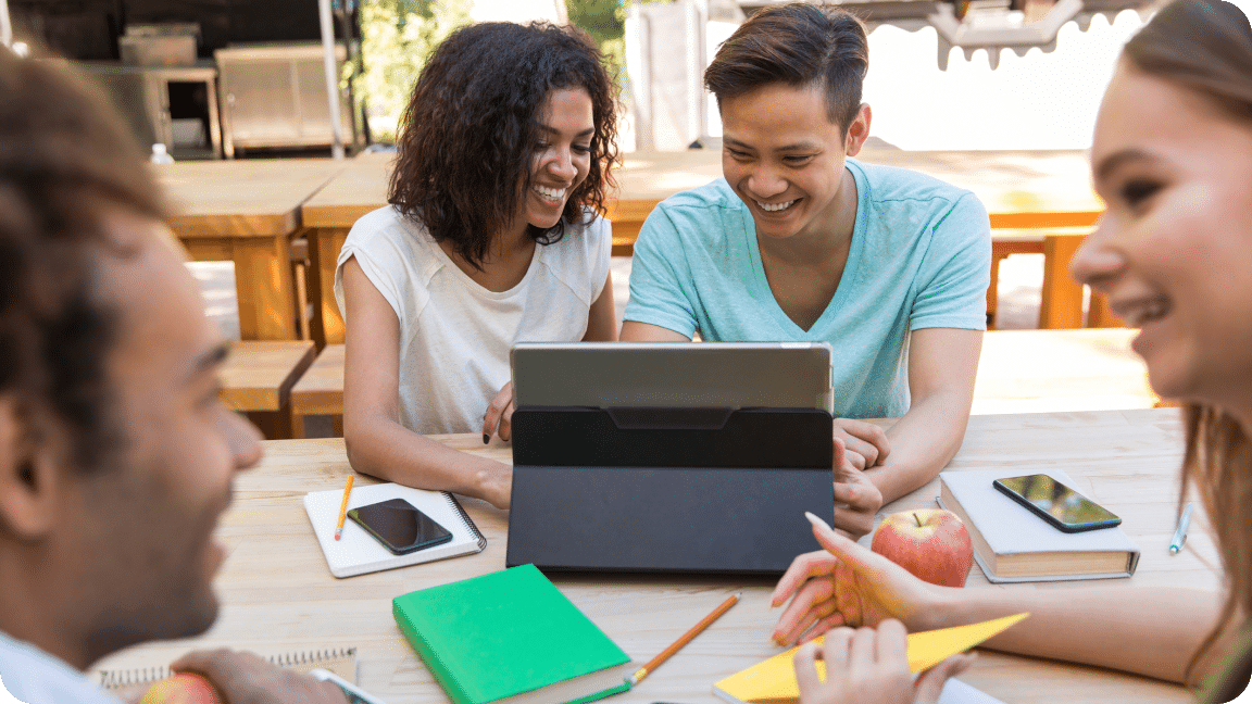 A table surrounded by a group of people, with two looking at a laptop.