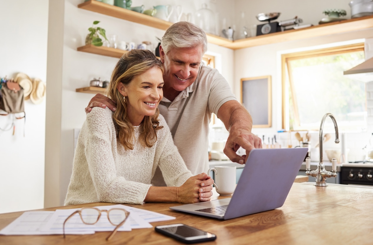 A couple scrolls through a website on their laptop in their kitchen.
