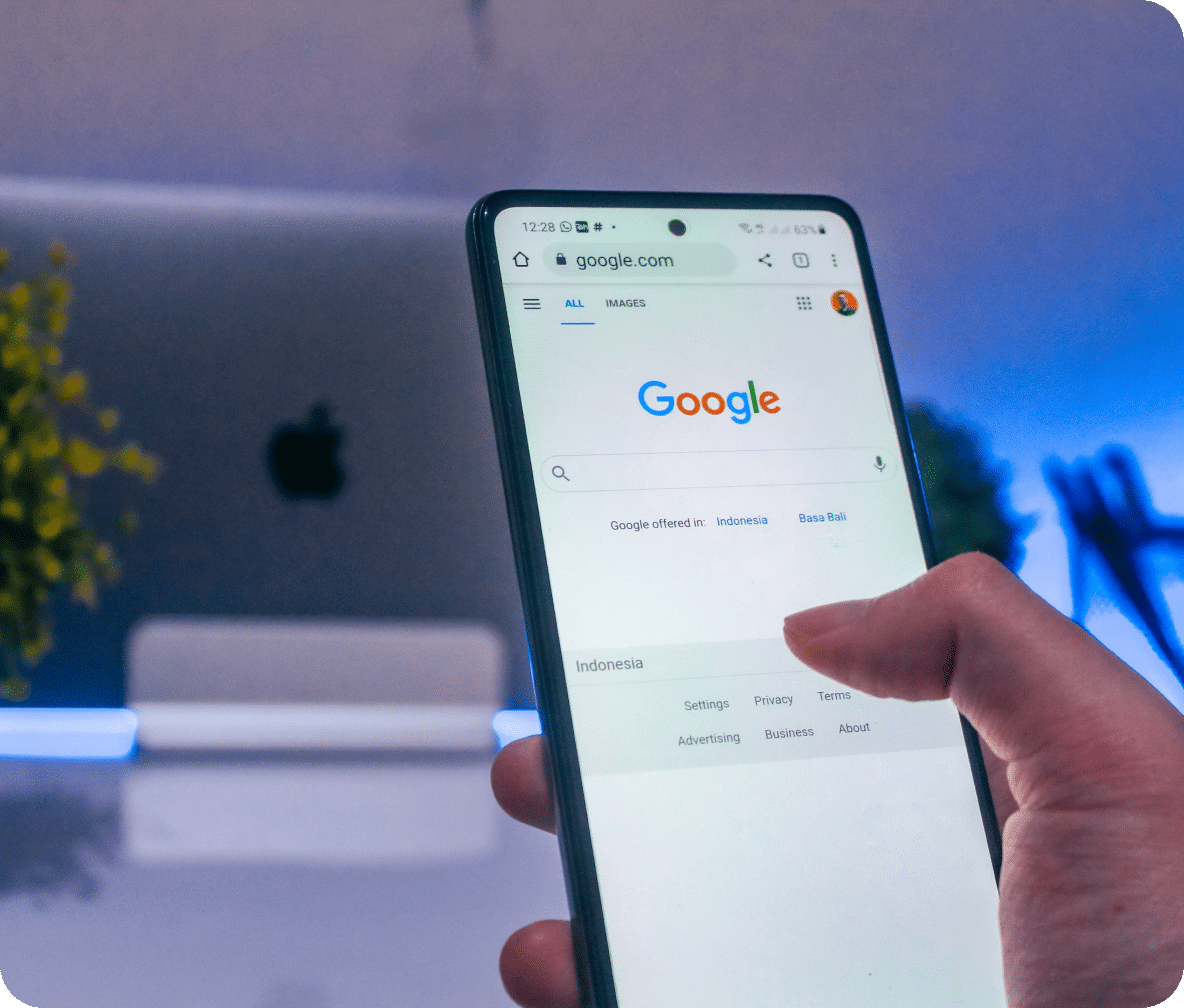 One hand holding a mobile phone, with the thumb clicking on the Google search page.