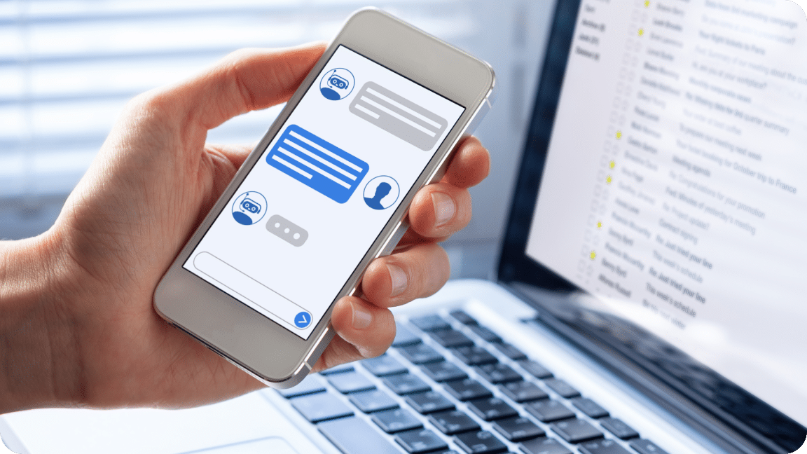 Person holds their phone with one hand, laptop in the background, as a chat bubble is displayed in the app.