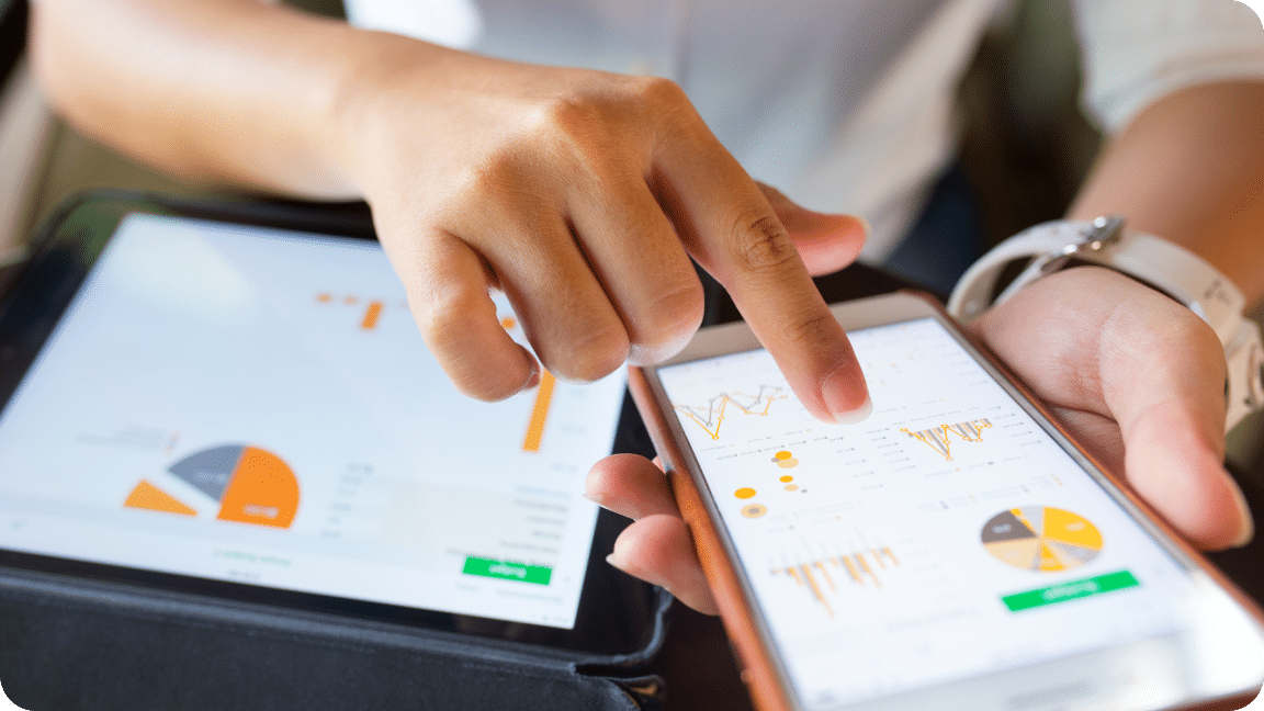 Tablet lays on a person lap, while they hold their mobile phone in their hands, looking at metrics and data on both.