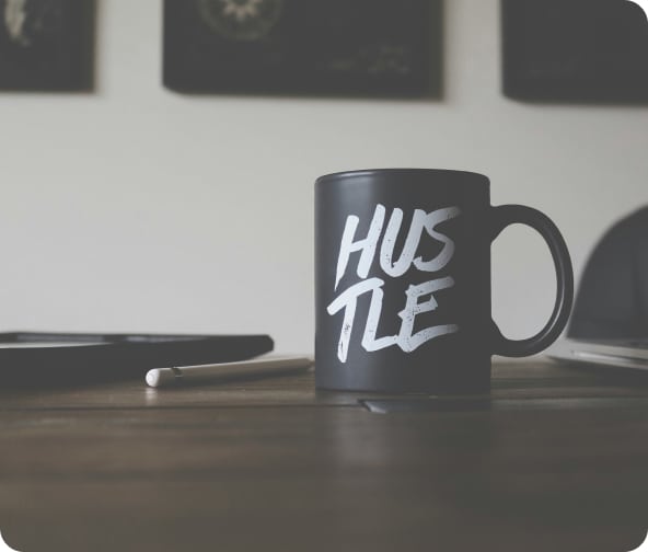 Black and white mug with "Hustle" in white, placed on a table with a tablet and drawing pen.