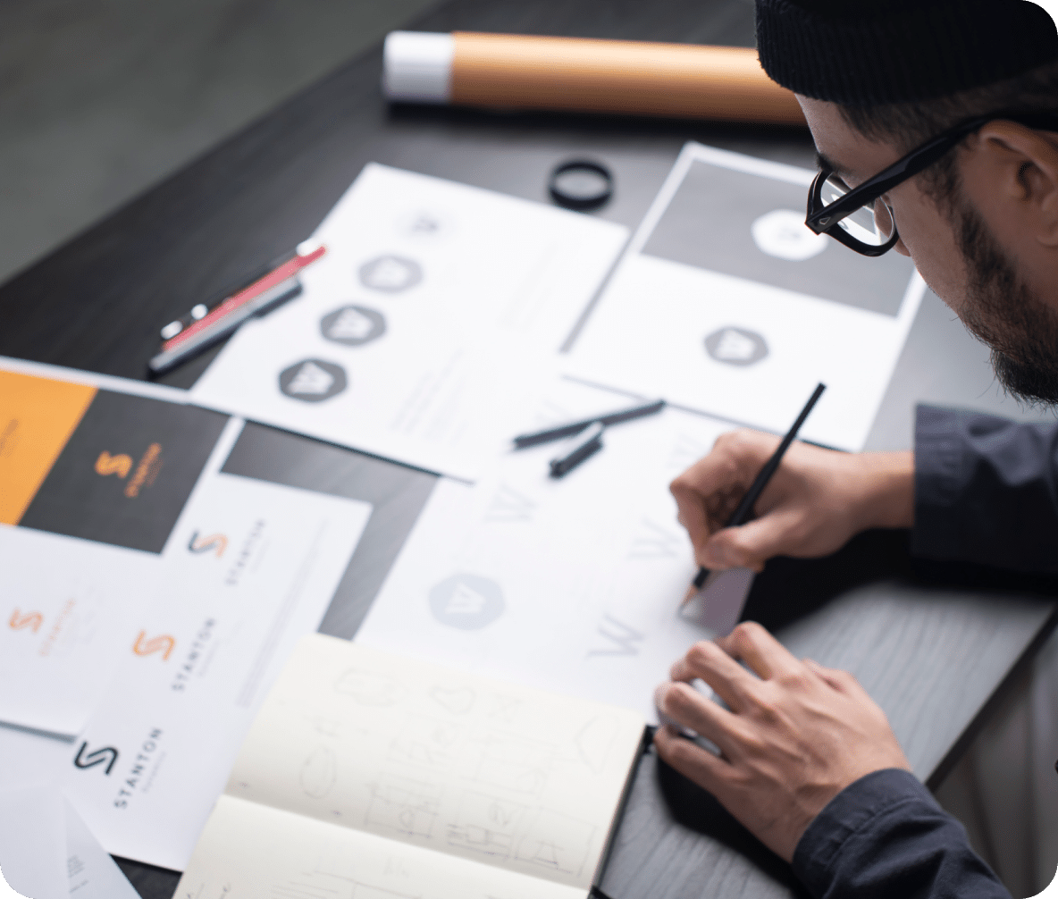 A person working with a bunch of papers having design versions with a lead pencil depicting efforts behind integrated designing services.