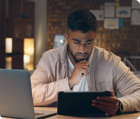 A person thinking while looking at the tablet with a laptop at a side on the table depicting ROI focused SEO done by Plan Left.