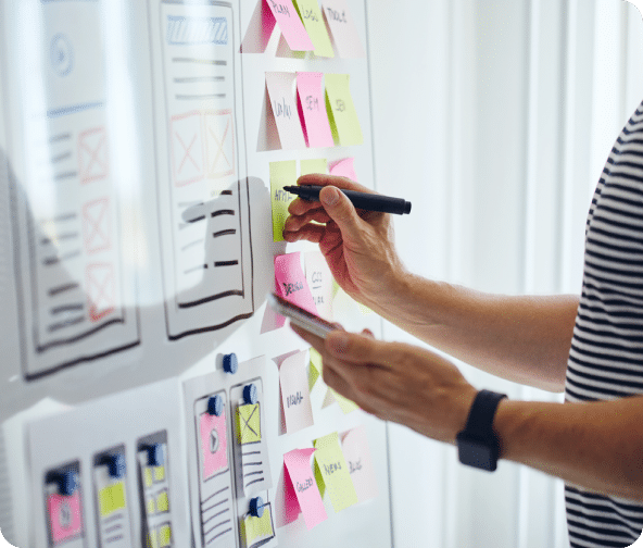 A whiteboard with several form layouts and sticky notes with a person writing something with a black marker depicting Strategic SEO.